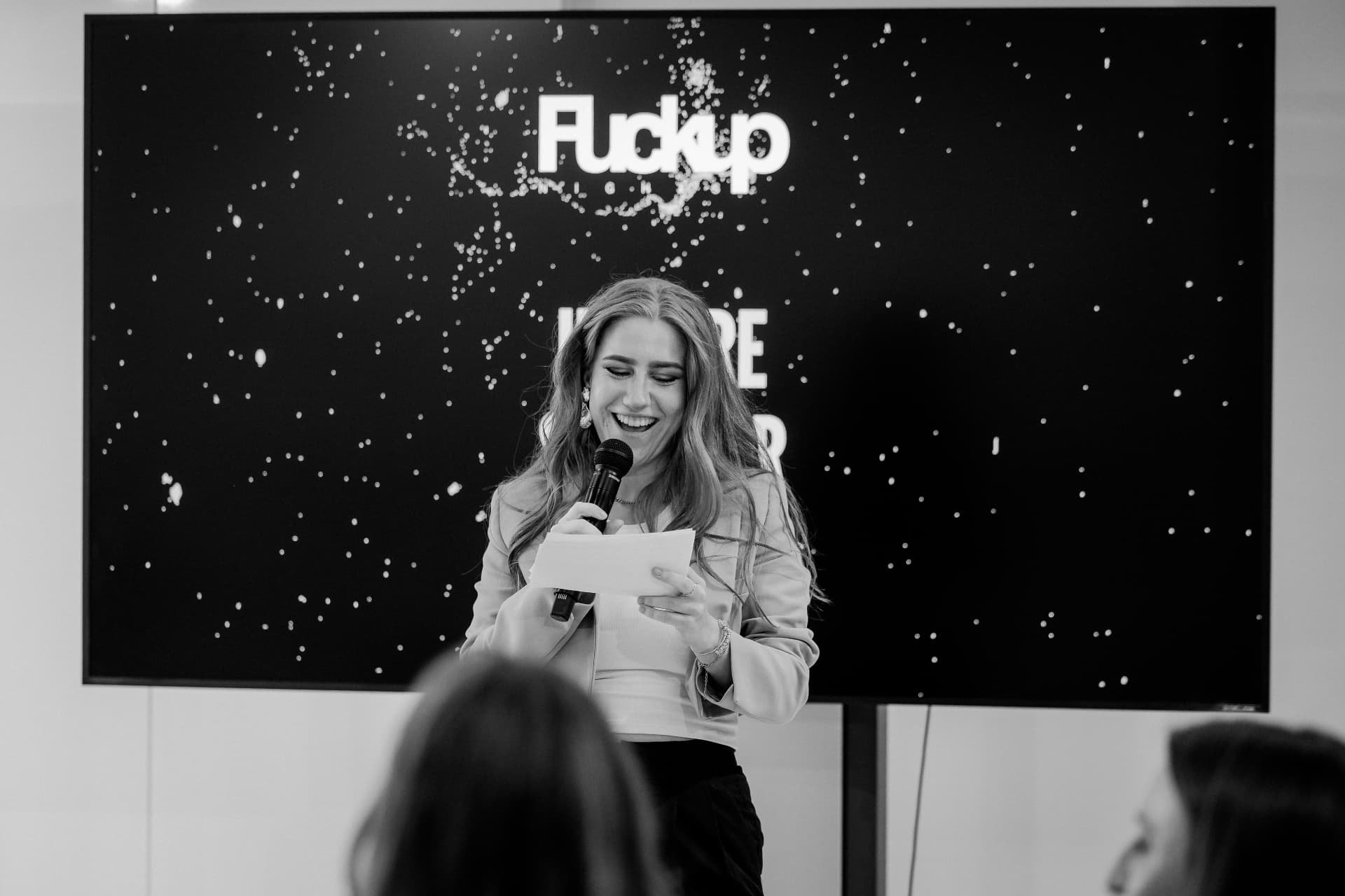 Black and white photo of Eva-Maria Schneider laughing while moderating FuckUp Night Graz