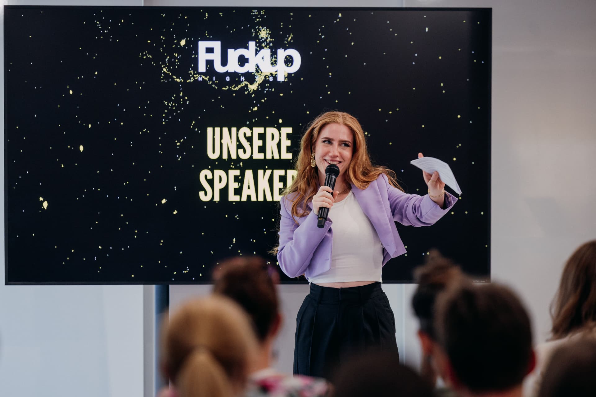 Eva-Maria Schneider hosting FuckUp Night Graz with a microphone in front of the speaker slide
